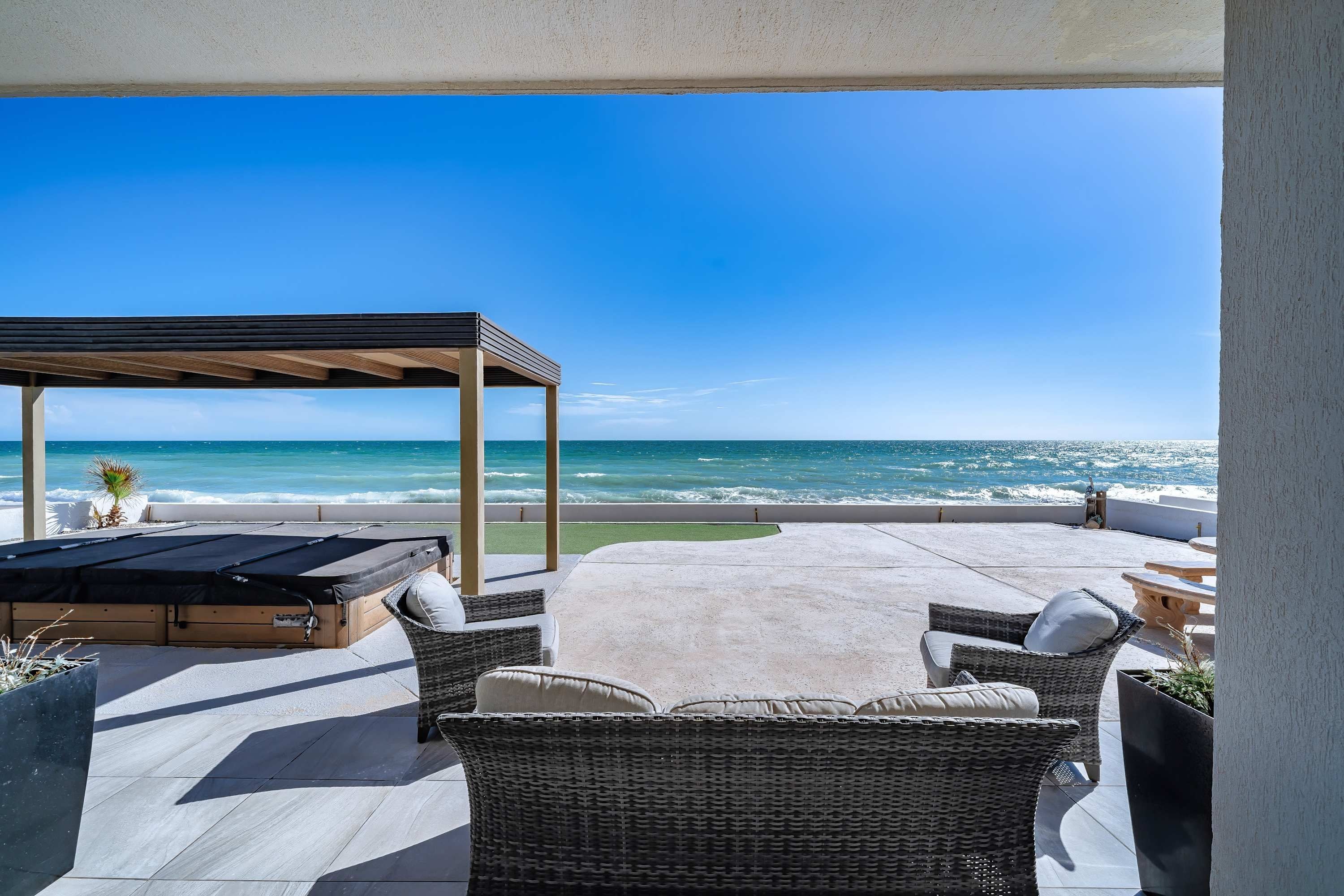 Un espace extérieur abrité, avec vue sur l’océan, comprenant une table de billard, des meubles en osier et une pergola.