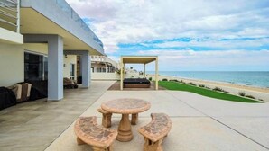 Une terrasse avec une table ronde et des bancs, un espace salon couvert et une vue sur la plage.