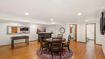 A spacious living room with a round dining table, wooden flooring, and a large window.