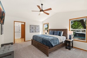 Une chambre à coucher comprenant un lit, un ventilateur de plafond, une fenêtre avec vue et une porte donnant sur la salle de bain.