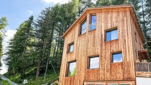 A wooden multi-story building with large windows and a balcony, surrounded by trees. - Arvenstudio by Interhome (La Punt-Chamues-ch)