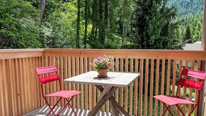 A wooden deck with a table and two red chairs, surrounded by a wooden railing. - Arvenstudio by Interhome (La Punt-Chamues-ch)
