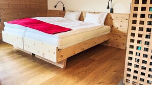 A wooden bed with a red blanket, white bedding, and two wall-mounted lamps. - Arvenstudio by Interhome (La Punt-Chamues-ch)