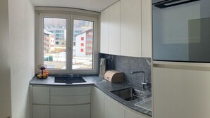 Eine kompakte Küche mit Einbauofen, Spüle und Fenster mit Blick auf Gebäude.