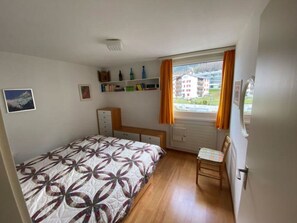 A bedroom with a bed, a chair, a desk, and a window with curtains. - Tgesa Piz Mez 24 Appartement/Fewo, Dusche, WC, 2 Schlafräume by Interhome (Savognin)
