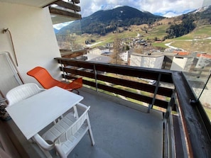 A balcony with a table and chairs, overlooking a mountainous landscape with buildings. - Tgesa Piz Mez 24 Appartement/Fewo, Dusche, WC, 2 Schlafräume by Interhome (Savognin)