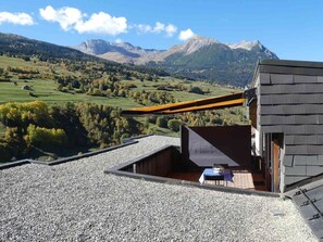 A modern building with a gravel roof, a wooden structure, and a table with a blue tablecloth. - Tgesa Sunnmatt Nr 46 Appartement/Fewo, Dusche, WC, 1 Schlafraum by Interhome (Savognin)