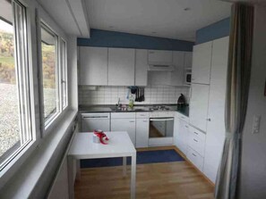 A compact kitchen with white cabinets, a small table, and a window. - Tgesa Sunnmatt Nr 46 Appartement/Fewo, Dusche, WC, 1 Schlafraum by Interhome (Savognin)