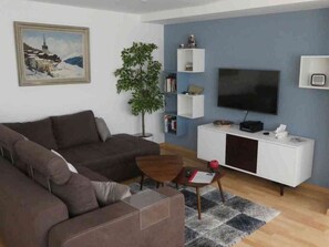 A living room with a sofa, a coffee table, a TV, a bookshelf, and a plant. - Tgesa Sunnmatt Nr 46 Appartement/Fewo, Dusche, WC, 1 Schlafraum by Interhome (Savognin)