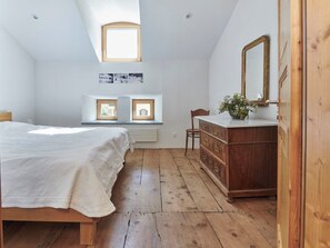 Ein Schlafzimmer mit Bett, Schminktisch, Spiegel und zwei Fenstern mit Bildern.