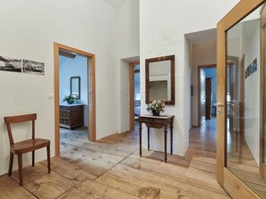 Ein Korridor mit Holzboden, einem Holzstuhl, einem kleinen Tisch mit einer Vase und einem Spiegel an der Wand.