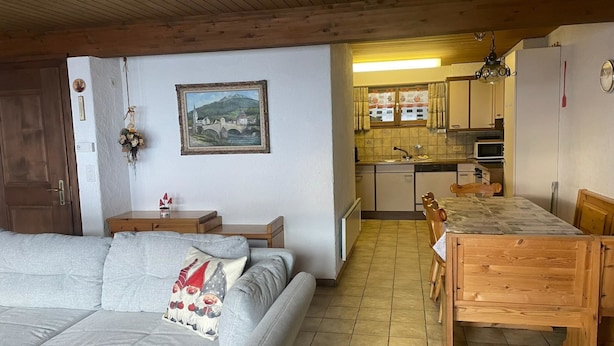 Uma sala de estar acolhedora com sofá, mesa de jantar e cozinha ao fundo.