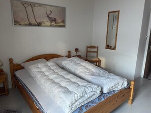 Una cama doble con estructura de madera, una mesita de noche con una lámpara, una silla, un espejo y un cuadro de un ciervo en la pared.