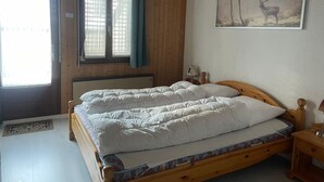 Quarto com cama de casal, janela com cortinas, radiador e quadro na parede.