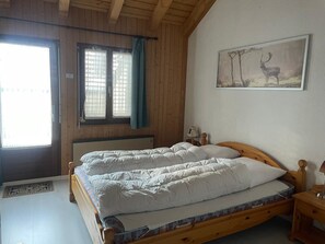 Ein Schlafzimmer mit einem Doppelbett, einem Fenster mit Vorhängen, einem Heizkörper und einem gerahmten Bild an der Wand.