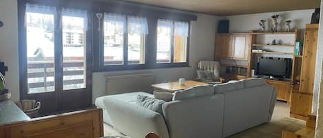 A cozy living room with a sofa, a wooden dining table, and a television.