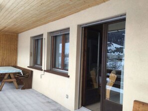 A room with a wooden ceiling, a table, and a view of a snowy landscape through a glass door. - Ferienhaus Somareiva Appartement/Fewo, Dusche oder Bad, WC, 2 Schlafräume by Interhome (Savognin)