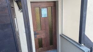 Uma porta de madeira com um painel de vidro, um tapete de entrada com desenho de abelha e uma pequena placa acima da porta.
