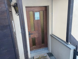 Eine Holztür mit Glasschiebeelement, eine Fußmatte mit einem Bienenmuster und ein kleines Schild darüber.