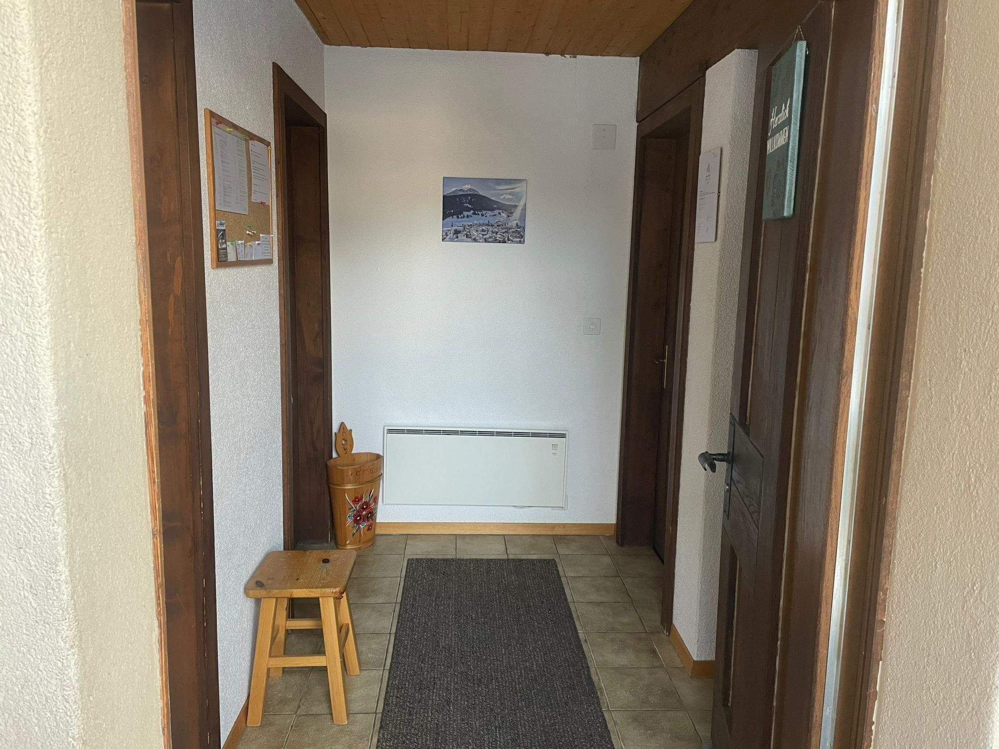 Un couloir étroit avec un banc en bois, un radiateur et une porte sur le côté droit.
