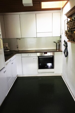 A compact kitchen with white cabinets, a stainless steel oven, and a coffee maker on the counter. - Penthouse Tgesa Tgampi T33 Appartement/Fewo, Bad, WC, 2 Schlafräume by Interhome (Savognin)