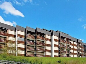 Ein mehrstöckiges Wohngebäude mit Balkonen, einer flachen Dachterrasse und blauem Himmel.