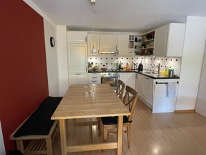 Una cocina compacta con armarios blancos, una mesa de comedor de madera y un horno empotrado.