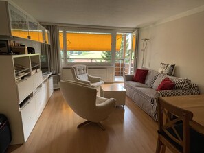 A modern living room with a sofa, armchair, and coffee table. There is a bookshelf and a window with a view. - Tgesa Sunnmatt Nr 11 Appartement/Fewo, Dusche, WC, 1 Schlafraum by Interhome (Savognin)