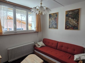 A room with a red sofa, a radiator, a window with curtains, and two paintings on the wall. - Casa Fasciati Appartement/Fewo, Dusche, WC, 2 Schlafräume by Interhome (Bivio)