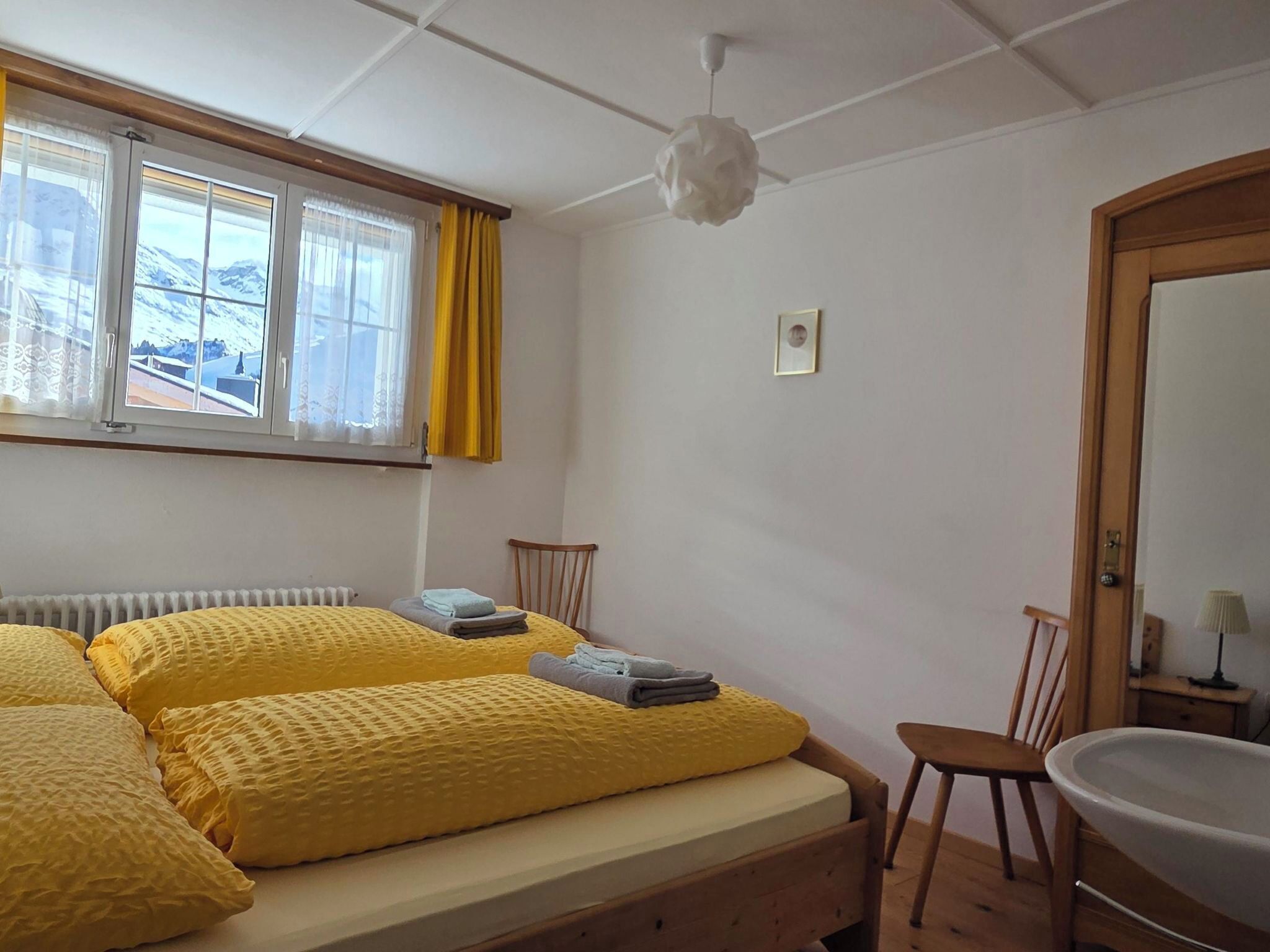 A room with a bed, a chair, a radiator, and a window with curtains.