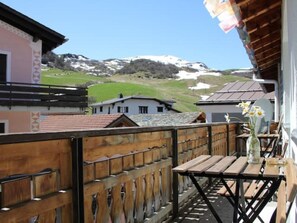 A balcony with a wooden railing, a table with a vase of flowers, and a view of snow-capped mountains in the background. - Casa Fasciati Appartement/Fewo, Dusche, WC, 2 Schlafräume by Interhome (Bivio)
