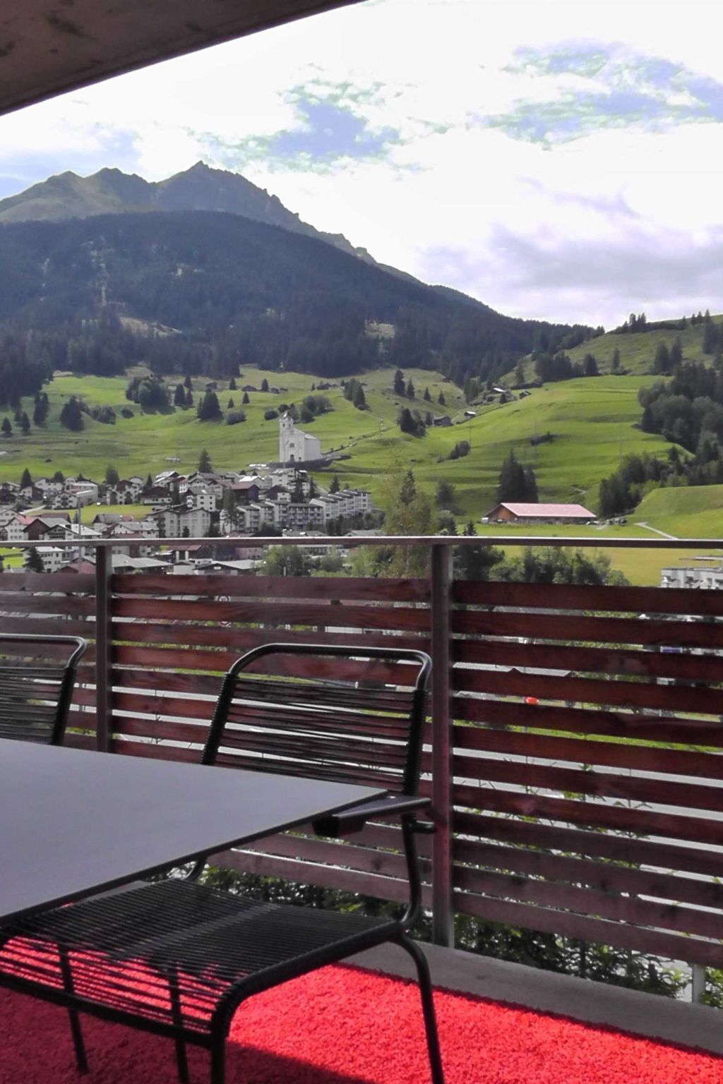 Un balcón con mesa y sillas, con vistas a un pueblo y montañas.