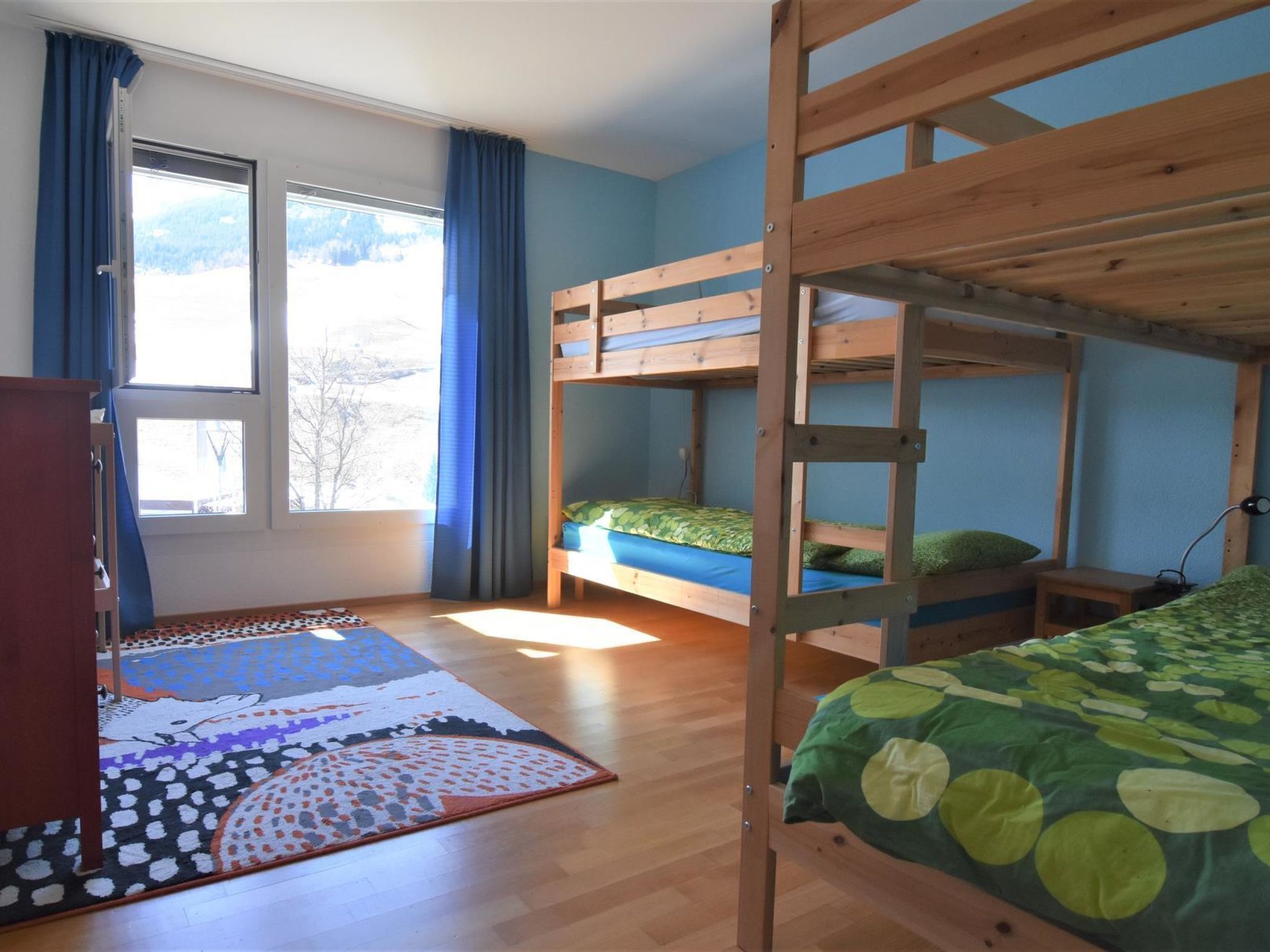 Una habitación con literas, una ventana con cortinas, un escritorio de madera y una alfombra estampada.