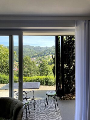 A room with a large sliding glass door leading to a balcony with a view of a forested valley. - Panoramic Apartment in the Black Forest, Prime Location, Terrace, Garden, Near Baden-Baden (Bühlertal)