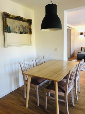 A dining area with a wooden table and chairs, a black pendant light, and a framed painting on the wall. - Panoramic Apartment in the Black Forest, Prime Location, Terrace, Garden, Near Baden-Baden (Bühlertal)