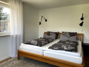 A double bed with a wooden frame, two bedside tables, a patterned bedspread, and a window with white curtains. - Panoramic Apartment in the Black Forest, Prime Location, Terrace, Garden, Near Baden-Baden (Bühlertal)