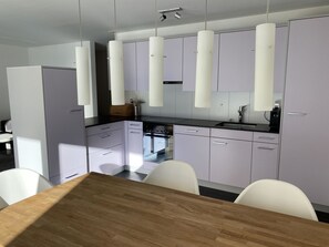Eine moderne Küche mit weißen Schränken, einem Holztisch und Pendelleuchten.
