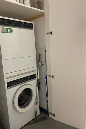 A compact laundry room with a front-loading washing machine, a drying rack, and a door.