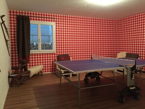 Ein Zimmer mit Tischtennisplatte, Fenster und einem Schachbrettmuster an der Wand.
