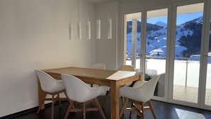 Un comedor moderno con una mesa de madera y sillas blancas, ventanas amplias con vista a la montaña.