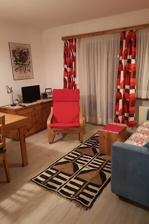A living room with a wooden desk, a red chair, a blue sofa, and a patterned rug.