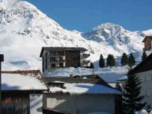 Un edificio moderno con varios balcones, rodeado de montañas nevadas y pinos.