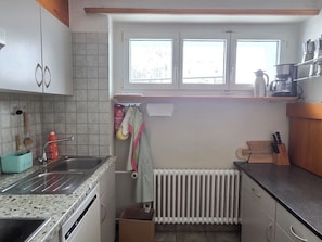 Et lille køkken med vask, bordplade og et vindue over radiatoren.