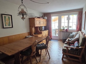 A dining area with a wooden table and chairs, a kitchen area with cabinets and a stove, and a seating area with a sofa and armchairs.
