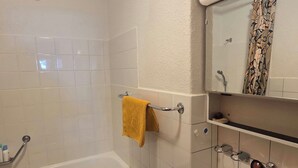 A bathroom with a bathtub, a shower, a towel rack with a yellow towel, a mirror, and a tiled wall. - Casa Fasciati Appartement/Fewo, Bad, WC, 4 oder mehr Schlafräume by Interhome (Bivio)