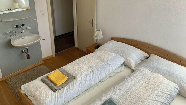 A bedroom with a single bed, a bedside table, a mirror, and a bathroom with a sink and towel rack. - Casa Fasciati Appartement/Fewo, Bad, WC, 4 oder mehr Schlafräume by Interhome (Bivio)