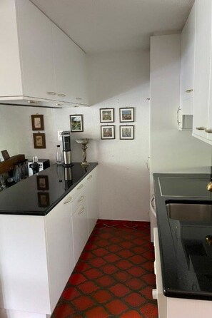 A compact kitchen with white cabinets, a black countertop, a red patterned floor, and a stove. - Haus Viols 54 Appartement/Fewo, Bad, WC, 2 Schlafräume by Interhome (Savognin)