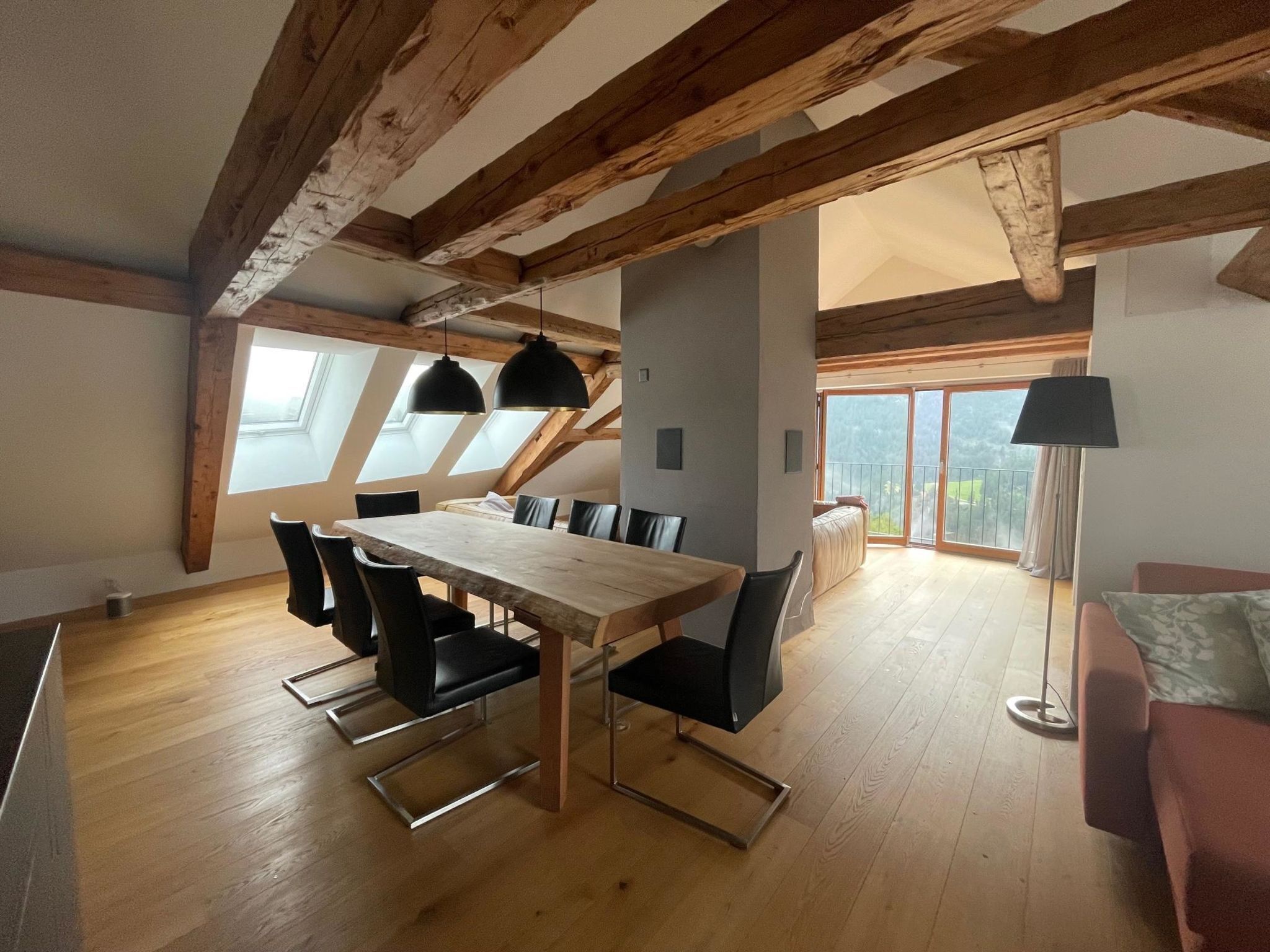A spacious dining area with a wooden table and chairs, large windows, and a view of the outdoors.
