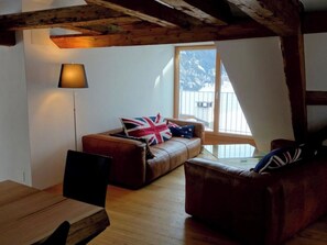 Un salon chaleureux, aménagé dans un style industriel, avec un plafond en bois, un canapé agrémenté d’un coussin à motifs Union Jack, un lampadaire et une vue sur un paysage enneigé par la fenêtre.
