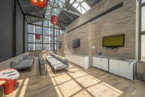A modern interior with a high ceiling, a seating area with sofas and a table, a kitchen area with a sink and cabinets, and a large window providing natural light. - Penthouse Loft, Central Downtown Dallas, Pool+Gym+Office, City Views (Dallas)